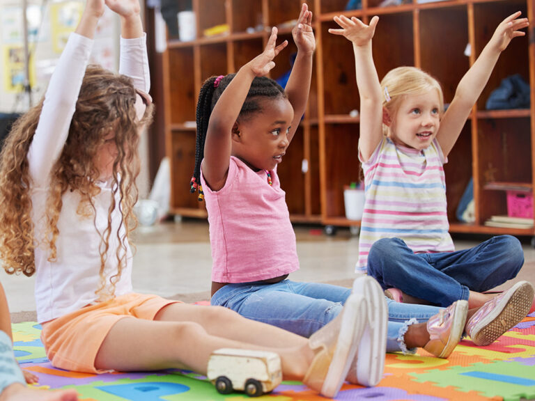 Three children raising their hands above their heads