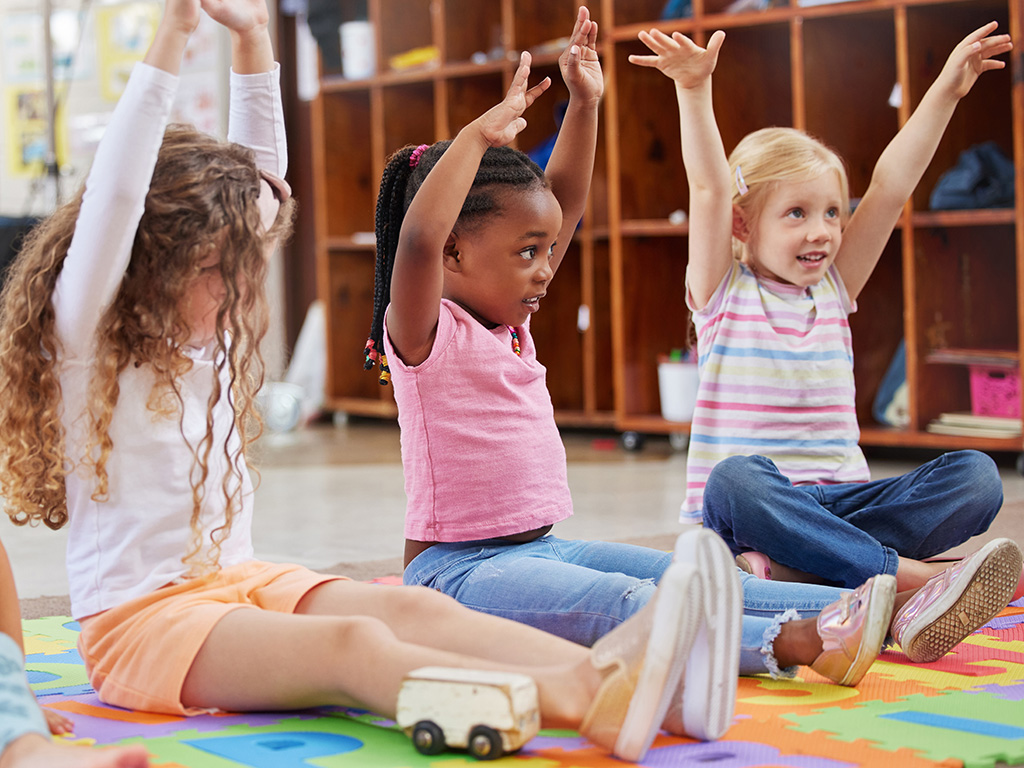Three children raising their hands above their heads